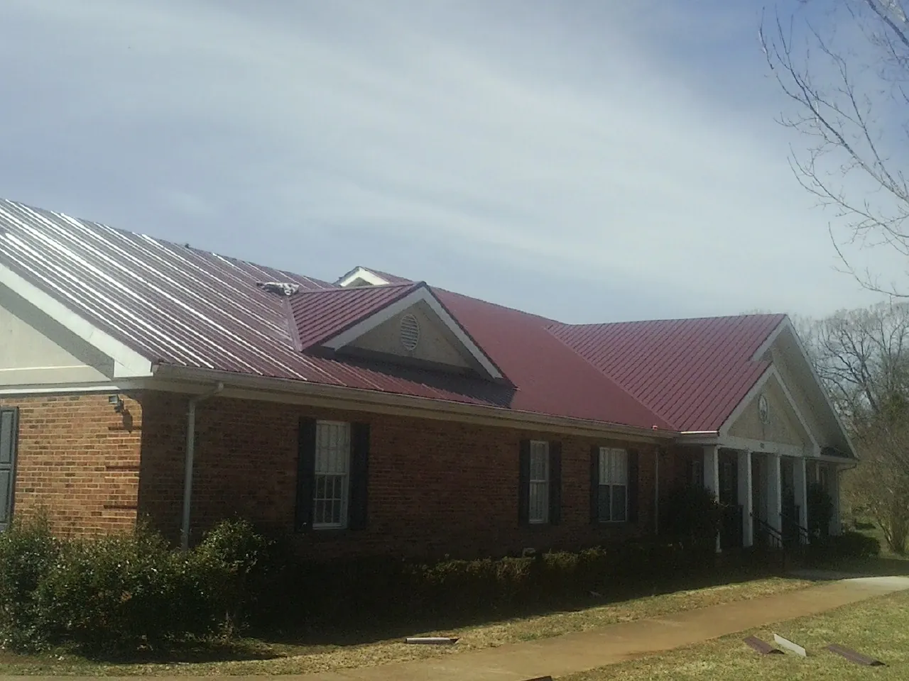 Red metal roof with gabled entries on a long brick building, from a Hail Damage Roof Repair job in Winthrop